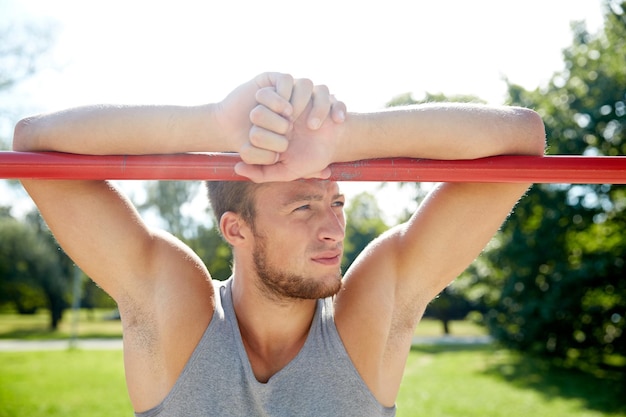 fitness, sport, training and lifestyle concept - young man exercising on horizontal bar outdoors