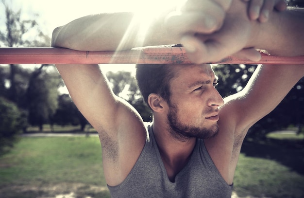 fitness, sport, training and lifestyle concept - young man exercising on horizontal bar outdoors