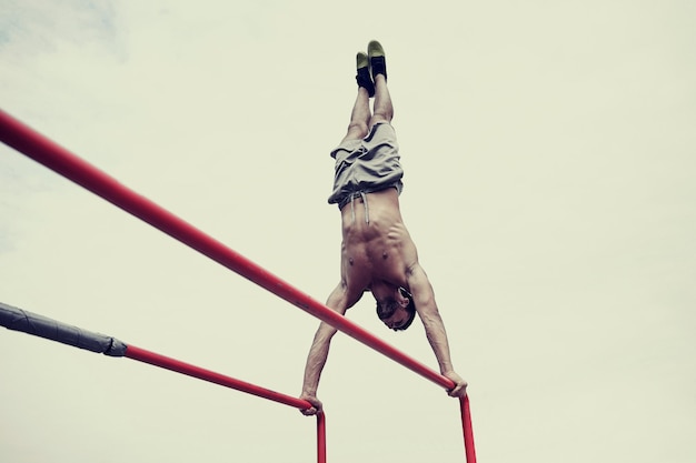 fitness, sport, training and lifestyle concept - young man exercising on parallel bars outdoors