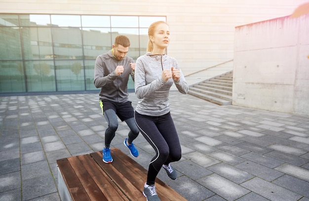 fitness, sport, training, people and lifestyle concept - couple making step exercise on city street bench