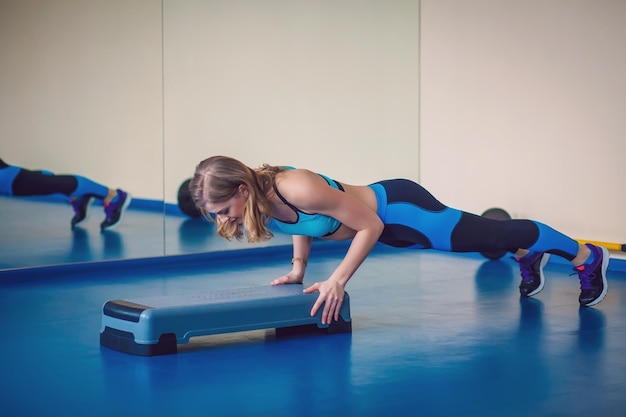 Fitness step, training, aerobics, sport concept - Athletic woman trainer at step doing aerobic class with steppers. Fitness woman with step platform doing workout in the gym. Sport conception.