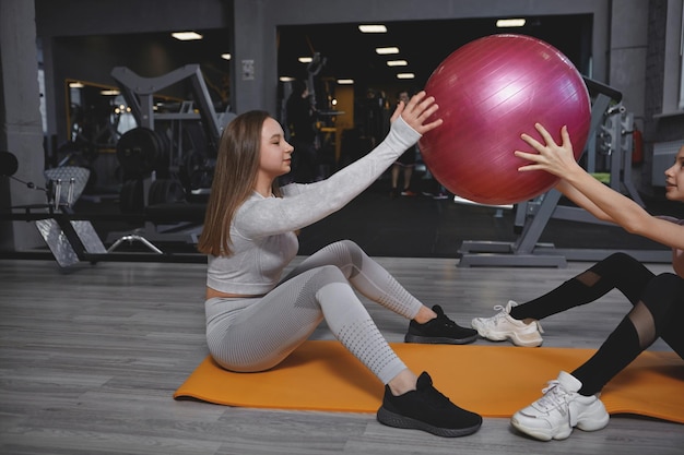 Fitness trainer exercising with her teen client doing fit ball sit ups