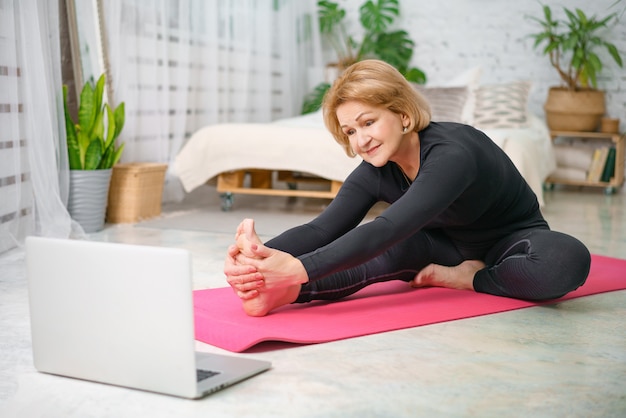 Fitness training online, senior woman at home with laptop.