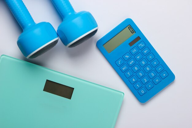 Fitness, weight loss still life. Calorie Counting. Calculator, dumbbells and scales on white. Minimalism. Flat lay