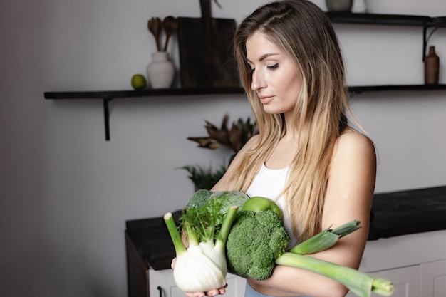 A fitness woman holds a full of fresh raw green vegetables