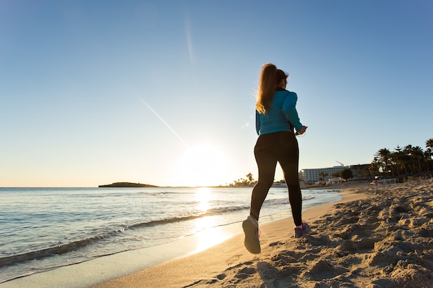 Fitness Woman Running by the Ocean at Sunset.