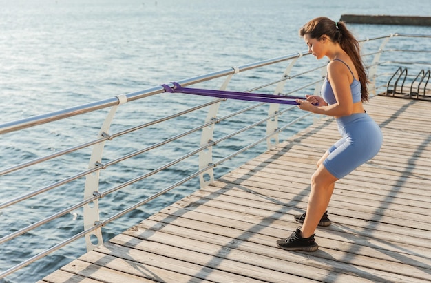 Fitness woman training muscles with fitness rubber bands on the beach