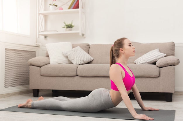 Fitness woman training yoga in cobra pose at home. Young slim girl makes exercise, copy space