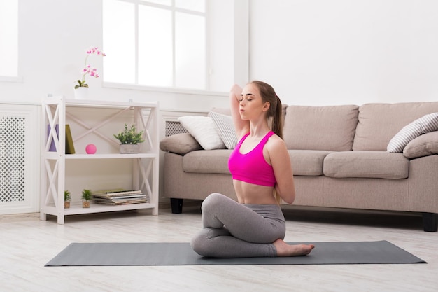 Fitness, woman training yoga in cow head pose at home. Young slim girl makes exercise.