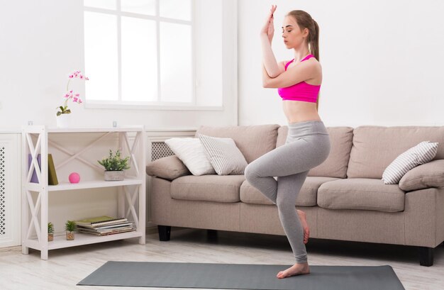 Fitness, woman training yoga in eagle pose at home. Young slim girl makes exercise.