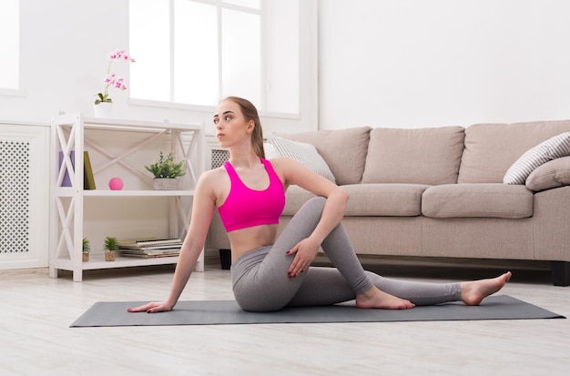 Fitness, woman training yoga in twisting sage pose at home. Young slim girl makes exercise.