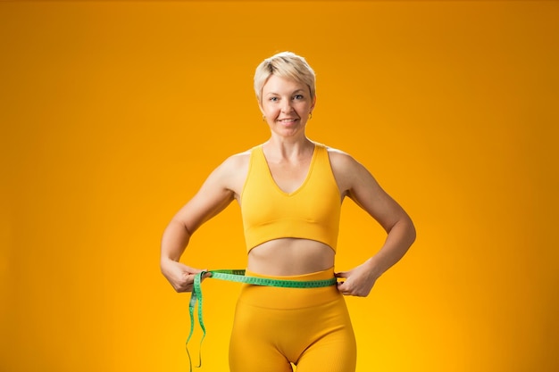 Fitness woman with measure tape isolated on yellow background Weight loss and healthcare concept