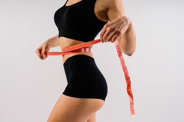 Fitness woman with tape measure showing her waist on studio background