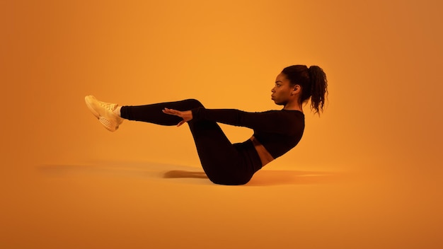 Fitness workout Active black lady doing abs exercises lying on floor over orange neon studio background side view