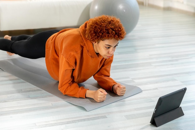 Fitness workout training young healthy fit african girl doing plank exercise on yoga mat on floor at