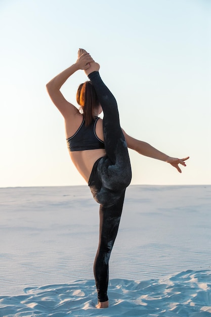 Fitness yoga woman stretching on sand. Fit female athlete doing yoga pose before running training outside in amazing landscape.