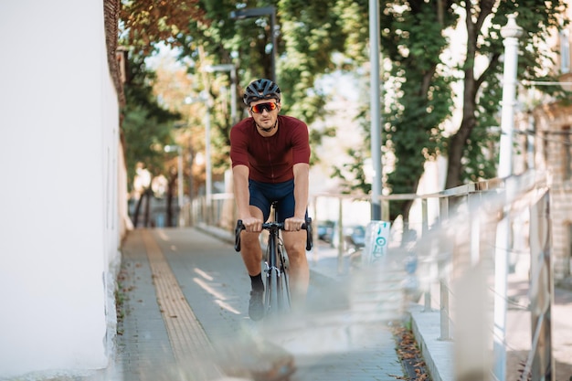 Fitness young man in safety helmet and sport glasses practicing in cycling outdoors Caucasian male person using black bike for training on city streets