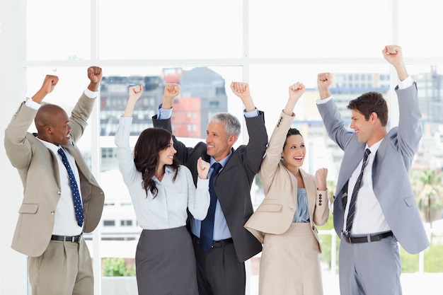 Five business people looking at each other and raising their arms in victory