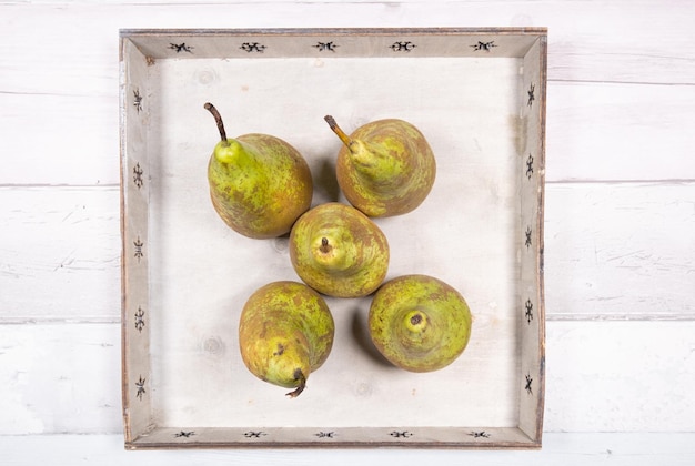 Five conference pears placed in an old wooden tray on an old wooden floor