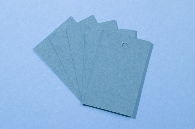 Five dark blue mat cardboard blank label tags for clothes with small holes in upper part put on each other resembling fan in center with shadows falling on bright blue background Tag mock up