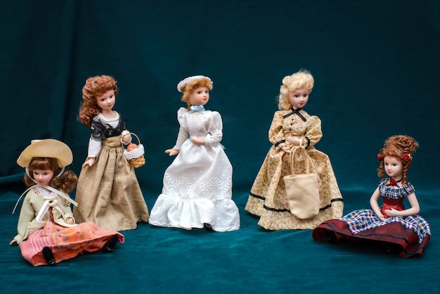 Five dolls in classic vintage dresses and hats on dark