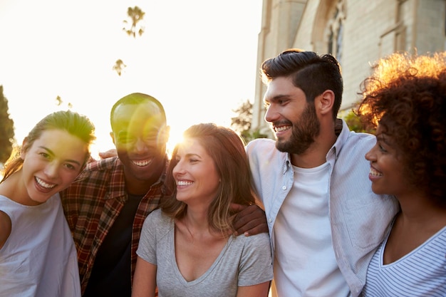 Five happy young adult friends embracing in the street