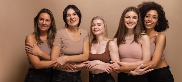 Five interracial pretty women in beige tops posing cheerfully together on brown background Lifestyle concept