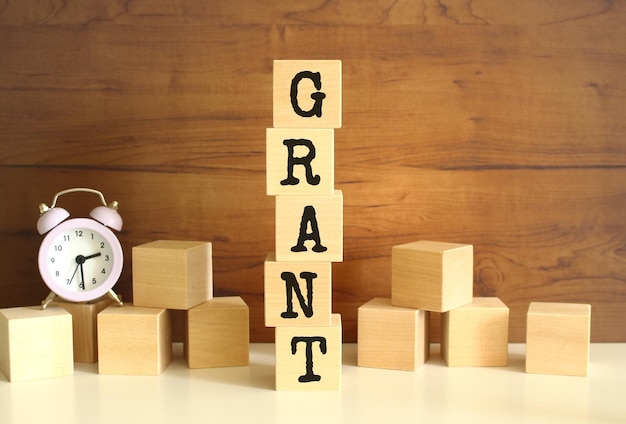 Five wooden cubes stacked vertically to form the word GRANT on a brown background