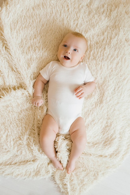 Fivemonthold baby is lying on a light blanket in the bedroom Top view of a charming boy