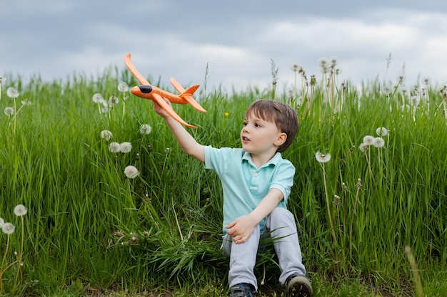 A fiveyearold boy sitting in a green meadow launches a toy airplane