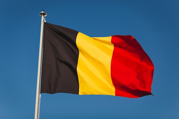 Flag of Belgium on mast. National flag against wind blue sky. Flag of Belgium, capital Bruxelles