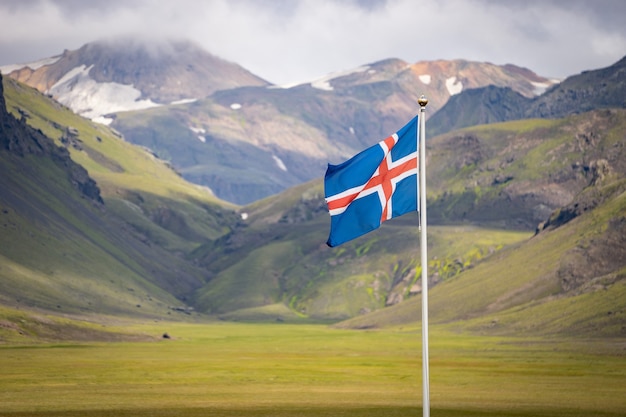 Flag of Iceland against the  of green mountains and blue sky.