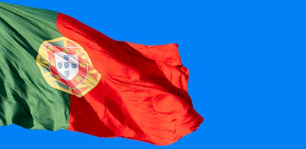 Photo flag of portugal in the wind on the blue sky background .