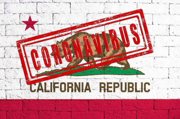 Flag of the State of California painted on grungy brick wall background with stamp CORONAVIRUS