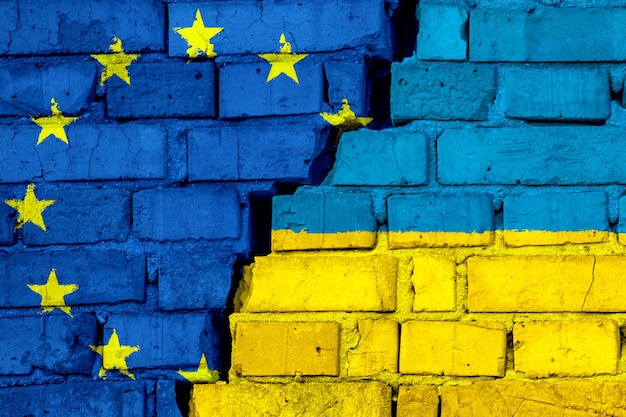 Flags of European union EU and Ukraine on the brick wall with big crack in the middle