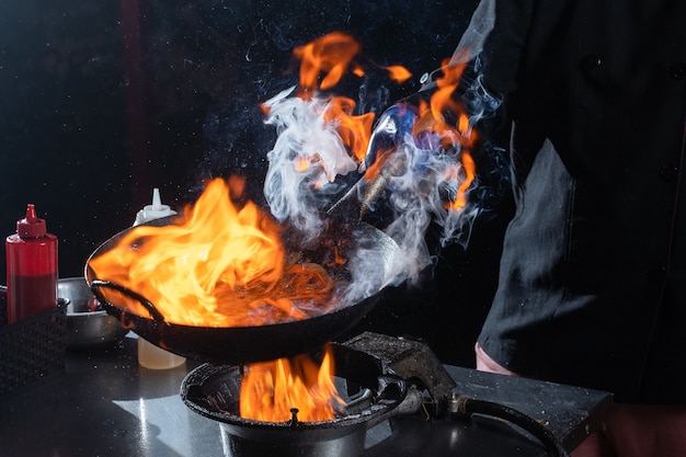 Flambe frying pan wok, cooking on fire. Pan-Asian cuisine. Street food.