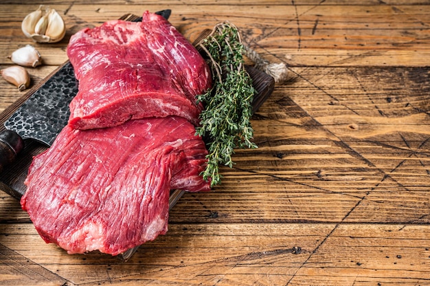 Flank raw beef steaks on a butcher cutting board with knife. wooden background. Top view. Copy space.