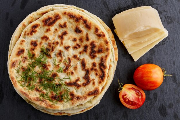 Flat bread with cheese and herbs and yoghurt sauce on a white plate on a dark stone table. View from above