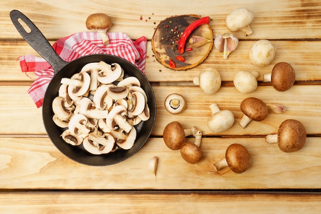 Flat composition with raw mushrooms cut into slices in a frying pan, on a wooden background