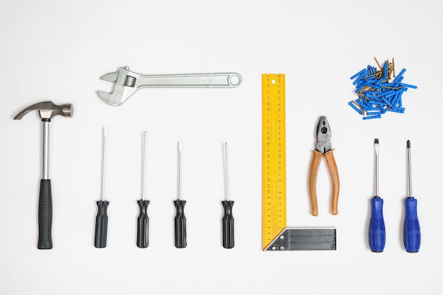 Flat lay of arranged screwdrivers with various tools and dowels with nails on white background