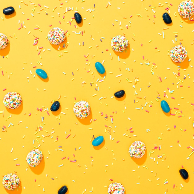 Flat lay arrangement of different colored candies on yellow background