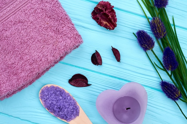 Flat lay arrangement of spa bathroom stuff on blue wood. Purple towel with candle and spoon.