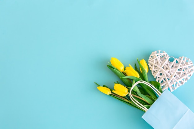 Flat lay blue background with yellow tulip flowers in a paper bag