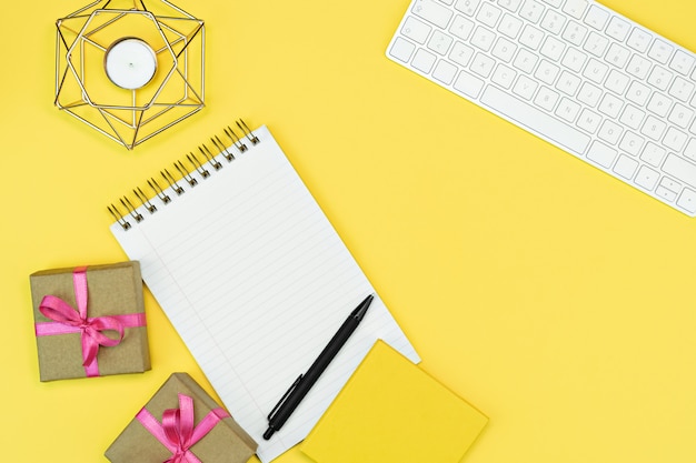 Flat-lay of bright yellow work space with key board note book and gift present boxes with pink ribbon, Yellow background