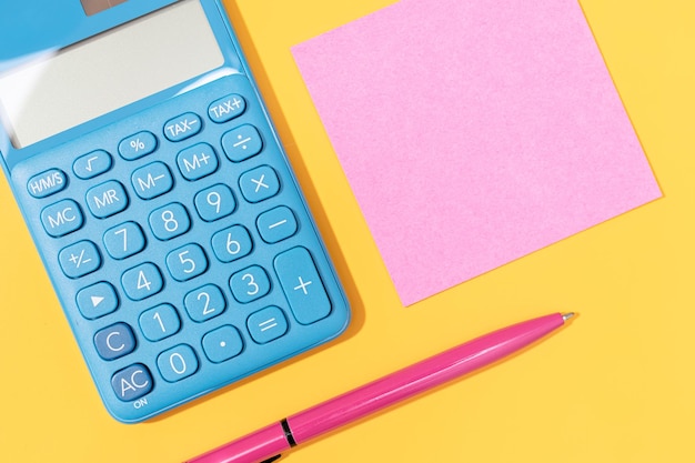 Photo flat lay of calculator pen and blank sticky note on yellow background vibrant colors mock up