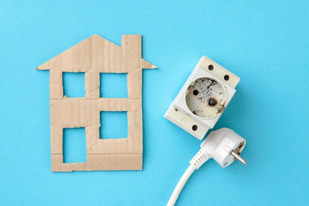 Flat lay of cardboard house and burnt electrical appliances of home power grid wire plug