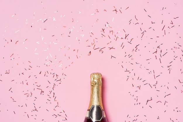 Flat lay of Celebration. Champagne bottle with colorful party streamers on pink background.