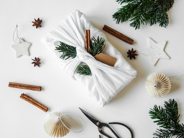 Flat lay Christmas fabric wrapped gift with paper tag, fir tree branch and cinnamon. Reusable sustainable gift wrapping alternative. Top view.