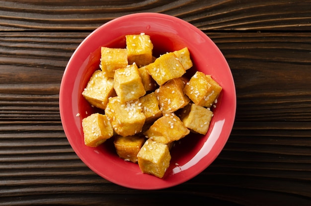 Flat lay closeup view at crispy deep stir fried tofu cubes with chives in clay dish on wooden kitchen table