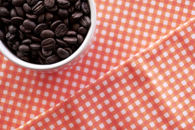 Flat lay of coffee beans in white ceramic cup on red tablecloth